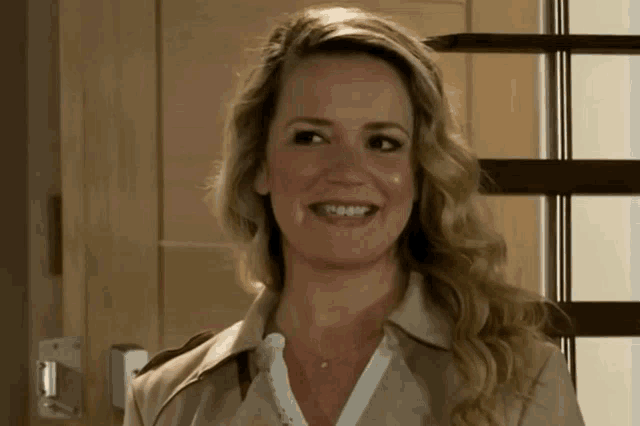 a woman in a tan trench coat is smiling