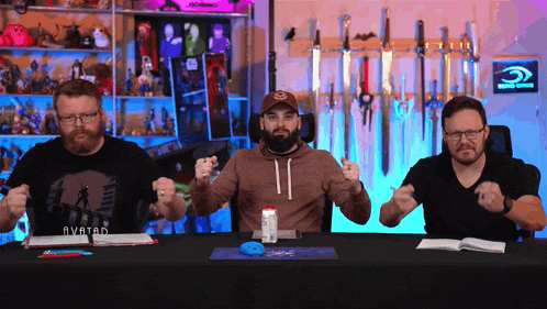 three men are sitting at a table and one has an avatar shirt on