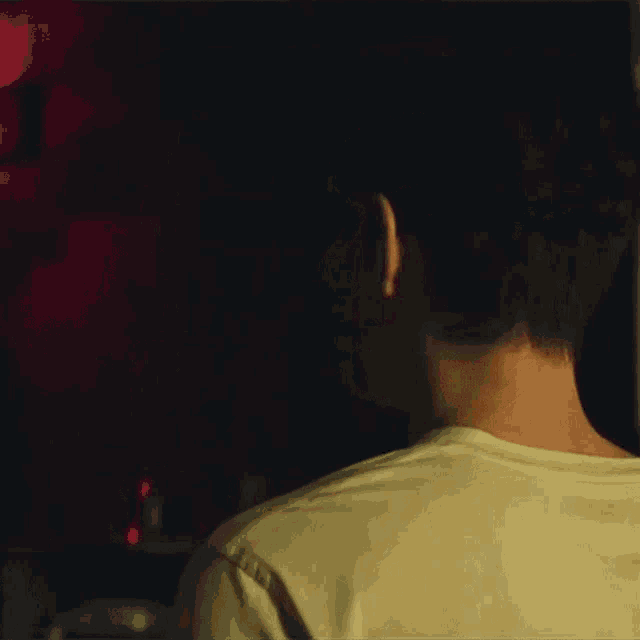 a man in a yellow shirt is looking over his shoulder at the camera in a dark room .
