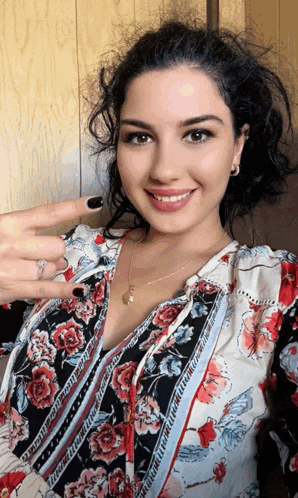 a woman wearing a floral shirt is smiling and pointing at her finger
