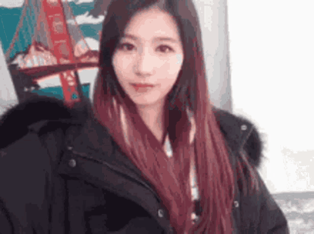 a young woman with long red hair is wearing a black jacket and looking at the camera .