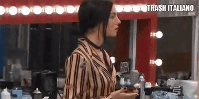 a woman in a striped shirt is standing in front of a mirror in a makeup room .