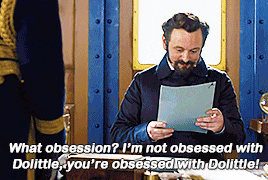a man with a beard is holding a piece of paper and says " what obsession ? "