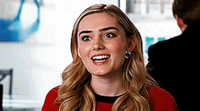 a blonde woman wearing a red sweater and earrings is smiling .