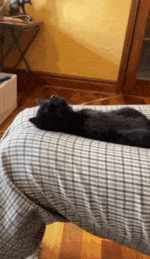 a black cat laying on a plaid blanket on a person 's leg