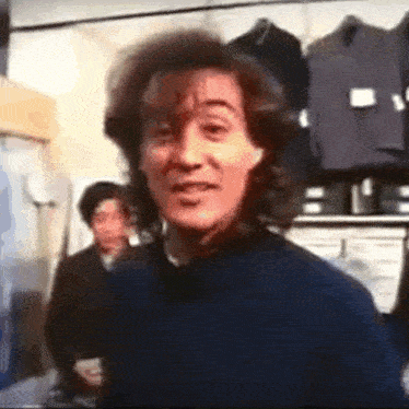 a man with curly hair is standing in front of a row of clothes .