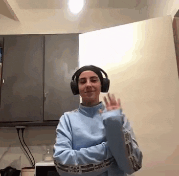 a woman wearing headphones and a blue sweatshirt is dancing in a kitchen .