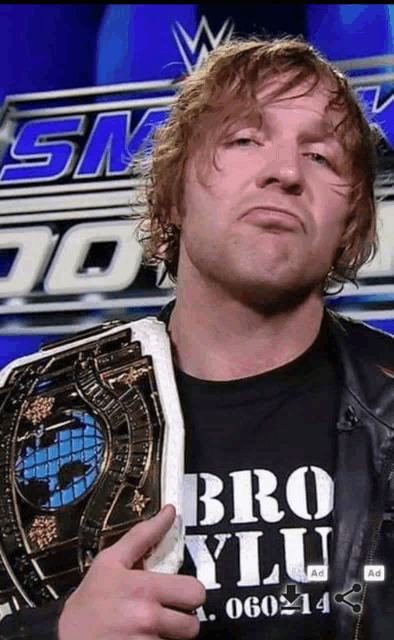 a man wearing a shirt that says bro ylu holds a wrestling championship belt