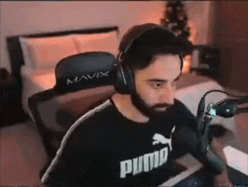 a man with a beard is wearing headphones and a puma shirt while sitting in a chair .