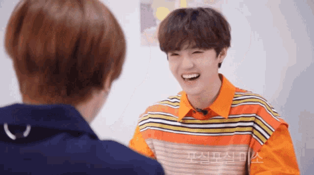 a man in a striped shirt is laughing with another man in a blue jacket
