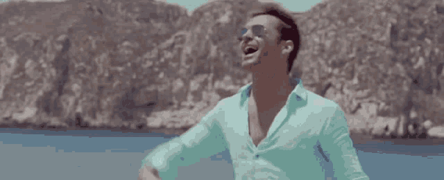 a shirtless man wearing sunglasses is laughing with his arms outstretched .