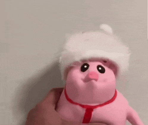 a person is holding a pink pig wearing a santa hat and a red tie .