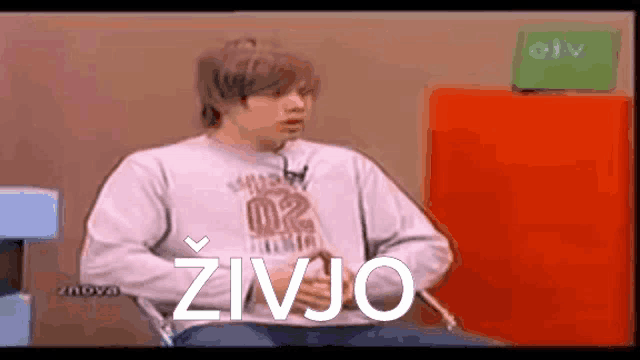 a man is sitting in a chair with the word zivjo written on the screen behind him .