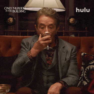 a man sitting on a couch drinking from a glass with a hulu ad behind him