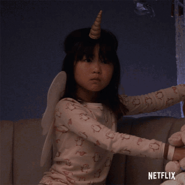 a little girl with a unicorn horn on her head is sitting on a couch with a netflix logo on the bottom