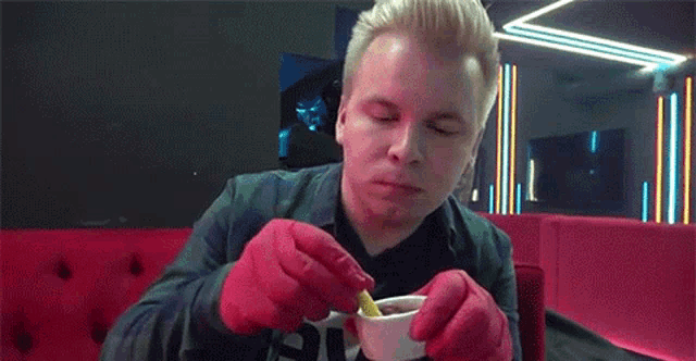 a man wearing red gloves is sitting at a table eating french fries .