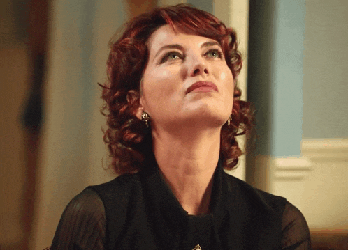 a woman with red hair is wearing a black top and earrings