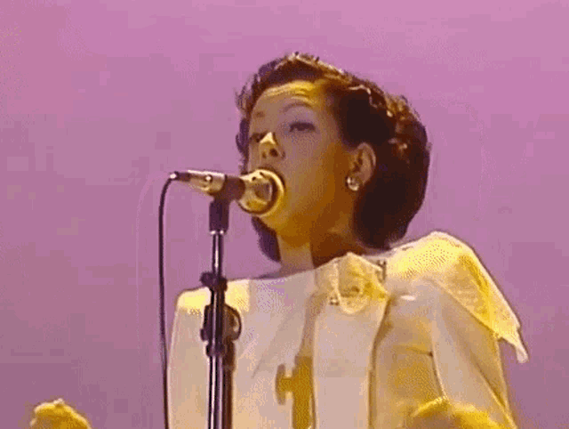 a woman is singing into a microphone while wearing a white shirt .