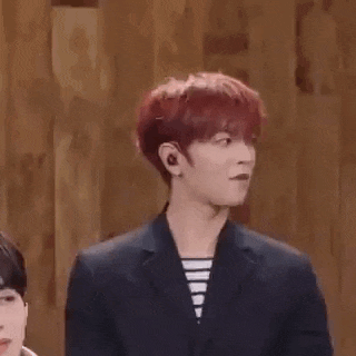 a man with red hair is wearing a suit and striped shirt and standing in front of a wooden wall .
