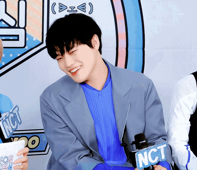 a man in a blue shirt is holding a microphone that says nct on it