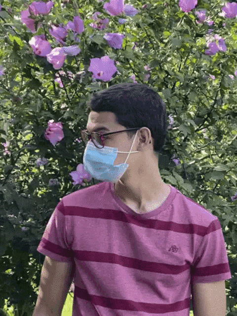 a man wearing a mask and glasses is standing in front of a bush with purple flowers