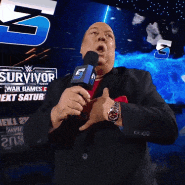a man in a suit is holding a microphone in front of a sign that says survivor