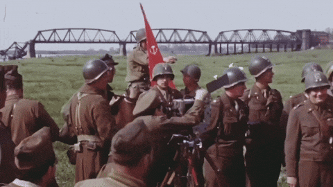 a group of soldiers are gathered in a field with a red flag in the background