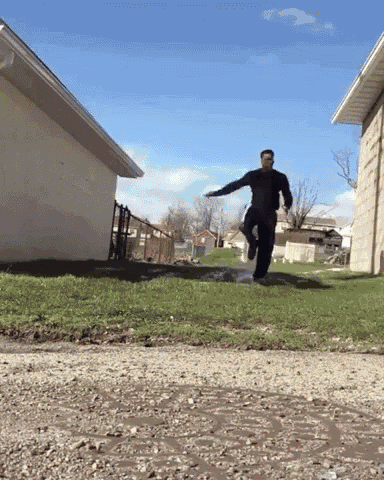 a man is jumping over a puddle on the side of a road