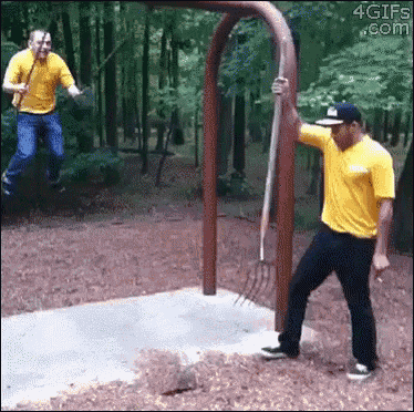 a man in a yellow shirt is holding a rake while another man jumps in the air behind him .