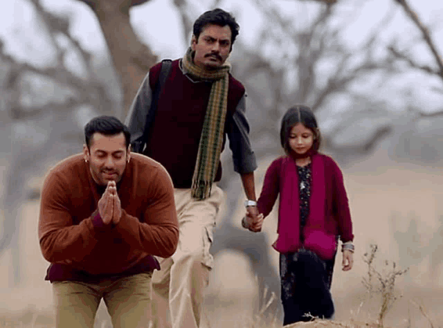 a man prays while holding a little girl 's hand in a field