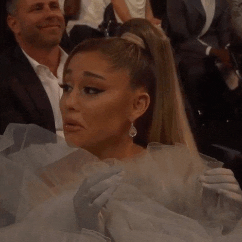 ariana grande is making a funny face while sitting in a crowd of people at an event .