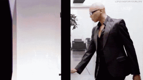 a bald man in a suit and glasses is standing in front of a glass door .