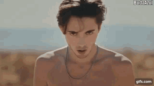 a shirtless young man wearing a necklace is standing in the desert .
