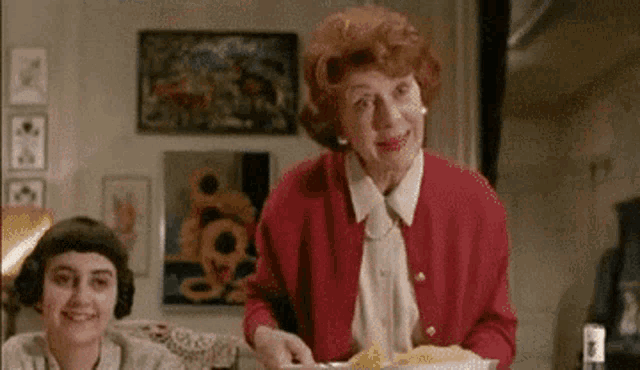 a woman in a red cardigan is holding a plate of food in front of a girl .