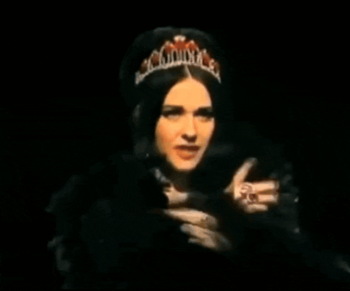 a woman in a black fur coat is pointing her finger at something in the dark .