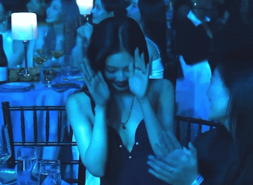 a woman covering her face with her hands while sitting at a table