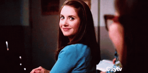 a woman in a blue shirt is smiling and looking over her shoulder while sitting at a table .