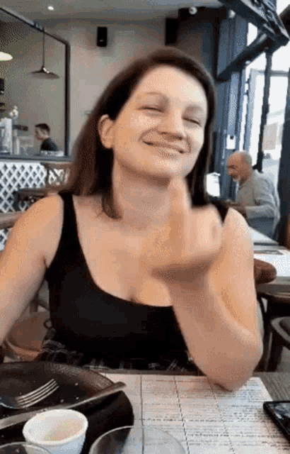 a woman in a black tank top is sitting at a table in a restaurant making a funny face
