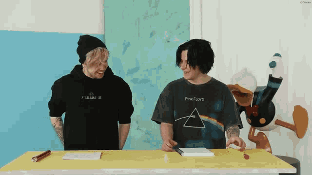 a man wearing a pink floyd shirt sits at a table with other people