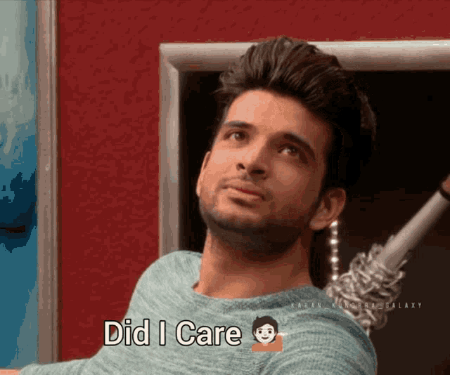 a man in a blue sweater says " did i care " in front of a red wall
