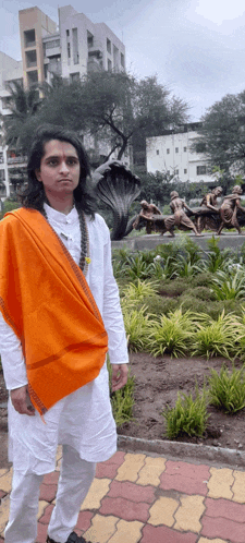 a man wearing a white shirt and an orange shawl stands in front of a statue