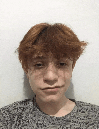 a young man with red hair is wearing a gray shirt with a pattern of letters including the letters a and e.
