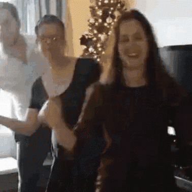 a group of women are dancing together in a living room in front of a christmas tree .