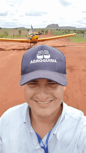 a man wearing a agroquima hat smiles in front of a plane