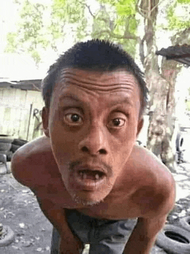 a shirtless man is making a funny face while standing in front of a pile of tires .