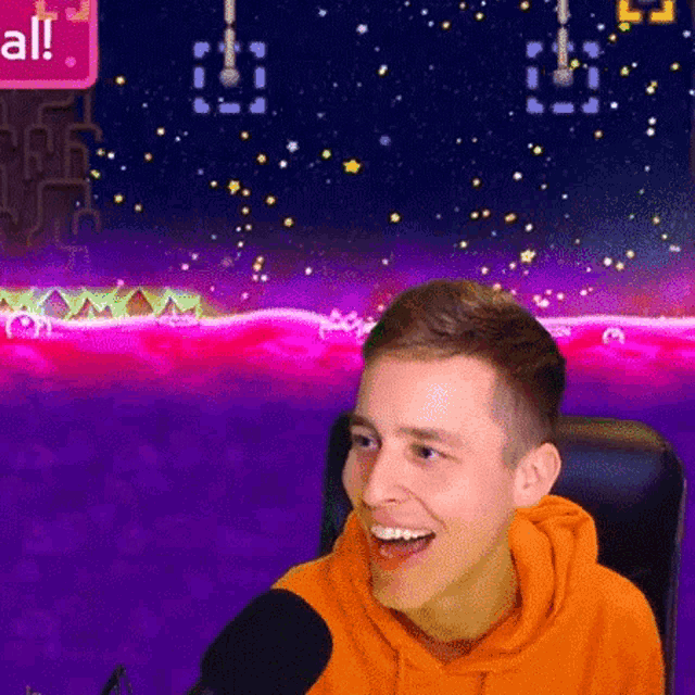 a man in an orange hoodie is sitting in front of a microphone in front of a video game background .