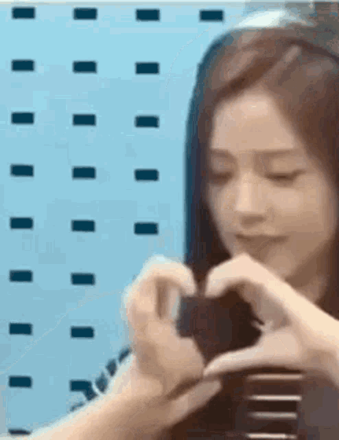 a woman is making a heart shape with her hands in front of a blue wall .