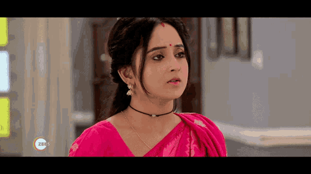 a woman in a pink saree with a red bindi on her forehead looks at the camera