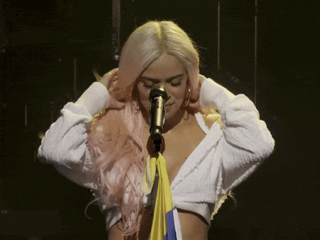 a woman with pink hair is singing into a microphone while covering her ears