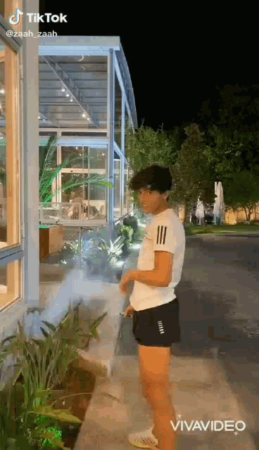 a young man in shorts is standing on a sidewalk in front of a building at night .